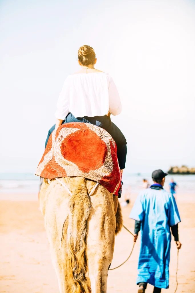 Private Morocco Tours – Tourist riding a camel on a Moroccan beach with local guide